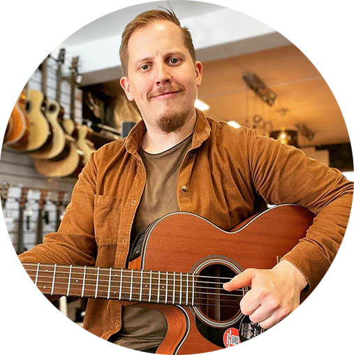 strg-S Webdesign mit Sinn Eine Person mit Bart hält eine Akustikgitarre in einem Musikgeschäft, umgeben von hängenden Gitarren. WordPress, Shopify