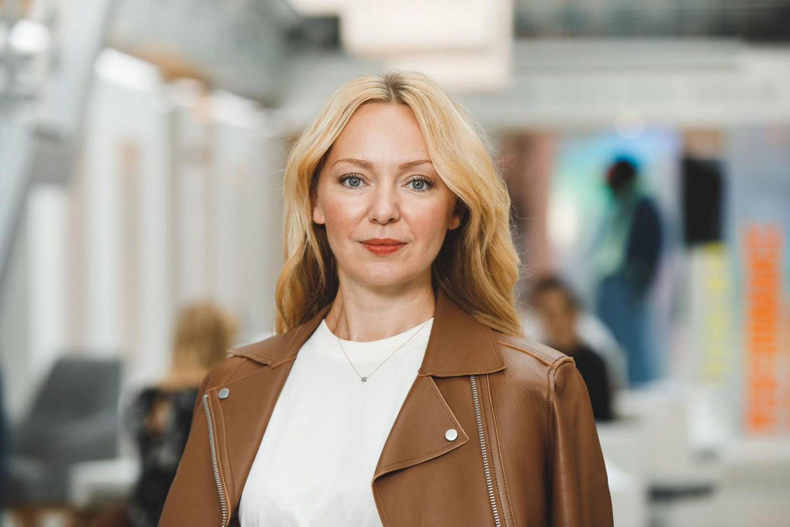 strg-S Webdesign mit Sinn Eine Person mit langen blonden Haaren, die eine braune Jacke und ein weißes Hemd trägt, steht in einem hell erleuchteten Innenbereich. WordPress, Shopify